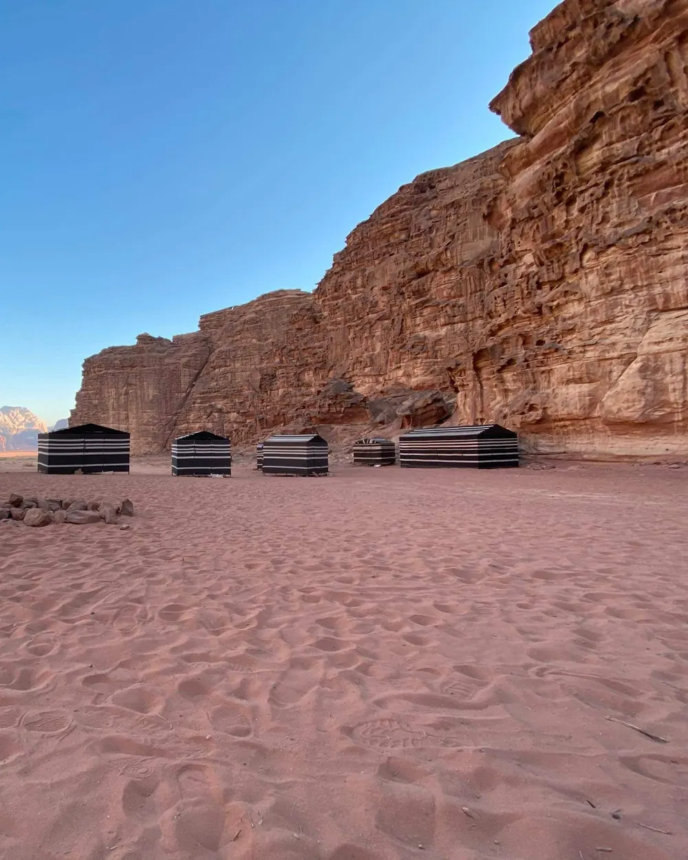 A row of striped Bedouin tents at the foot of a Wadi Rum cliff