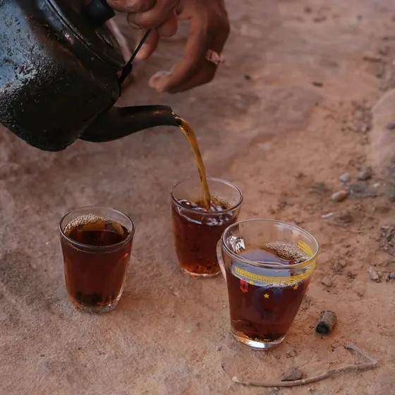 Bedouin tea poured from a blackened pot into small glasses on the sand