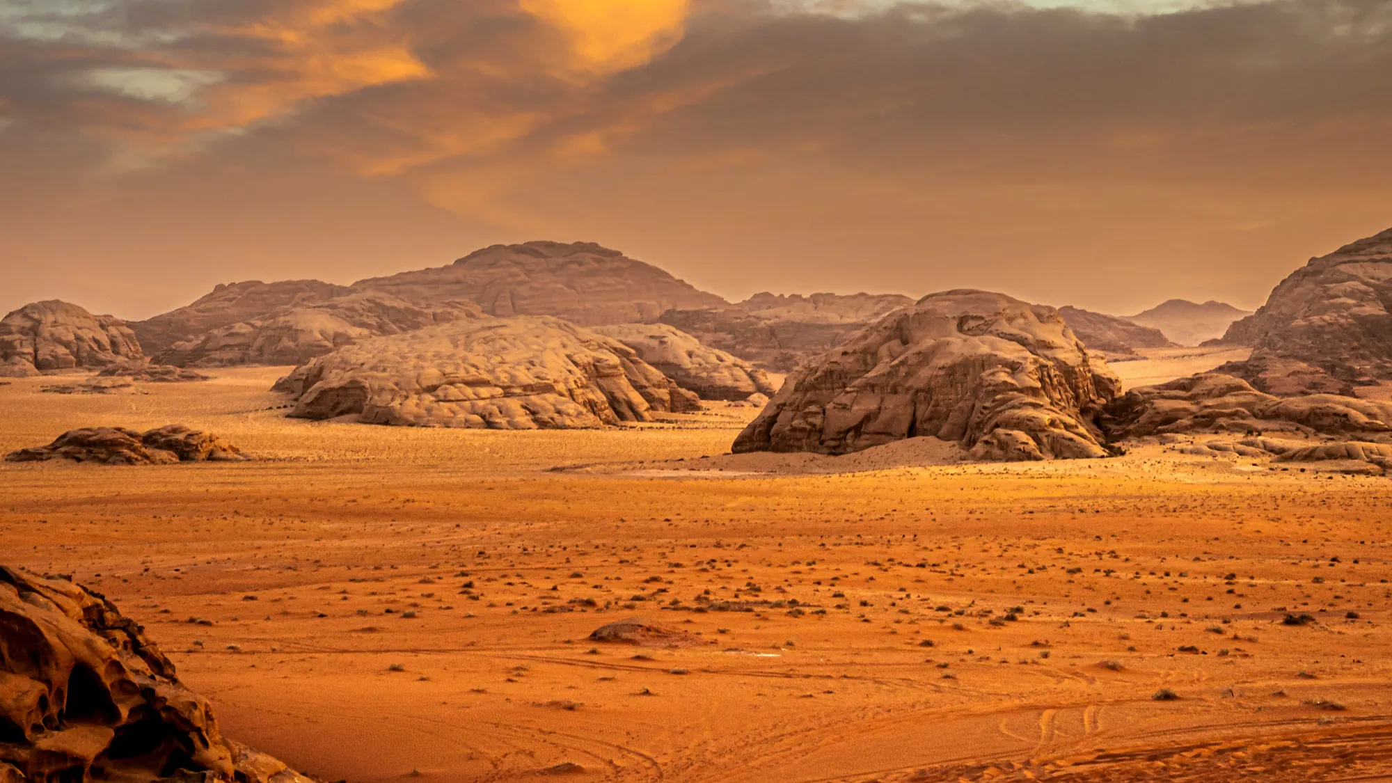 A sandy plain and rock domes in Wadi Rum under a golden evening sky