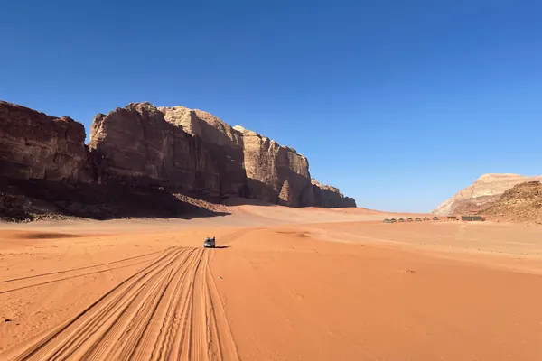 Tyre tracks across the red sand leading toward the cliffs
