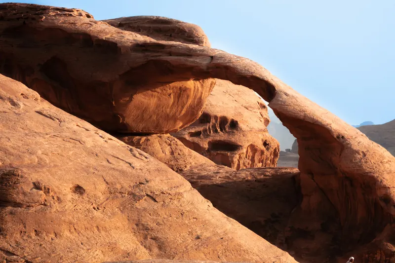 A natural sandstone arch with a person sitting beneath it